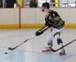 Roller hockey player in action on indoor rink, wearing a helmet and striped uniform, ready to hit the puck.