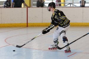 Roller hockey player in action on indoor rink, wearing a helmet and striped uniform, ready to hit the puck.