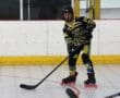 Roller hockey player with stick in action on indoor rink, wearing yellow and black gear.