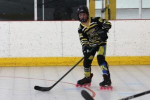 Roller hockey player with stick in action on indoor rink, wearing yellow and black gear.