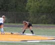 Two field hockey players compete intensely on a grass field during a sunny match.