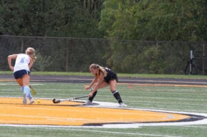 Two field hockey players compete intensely on a grass field during a sunny match.