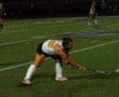 Field hockey player preparing to hit the ball during a night match.