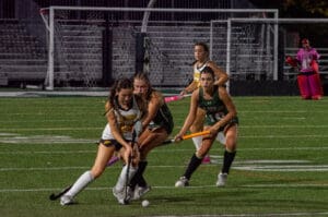 Girls playing competitive field hockey match under stadium lights.