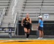 Female field hockey player running on track during practice near coach at sports stadium.