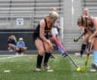 Two field hockey players compete for the ball during a game on a grassy field.