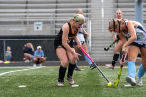 Two field hockey players compete for the ball during a game on a grassy field.