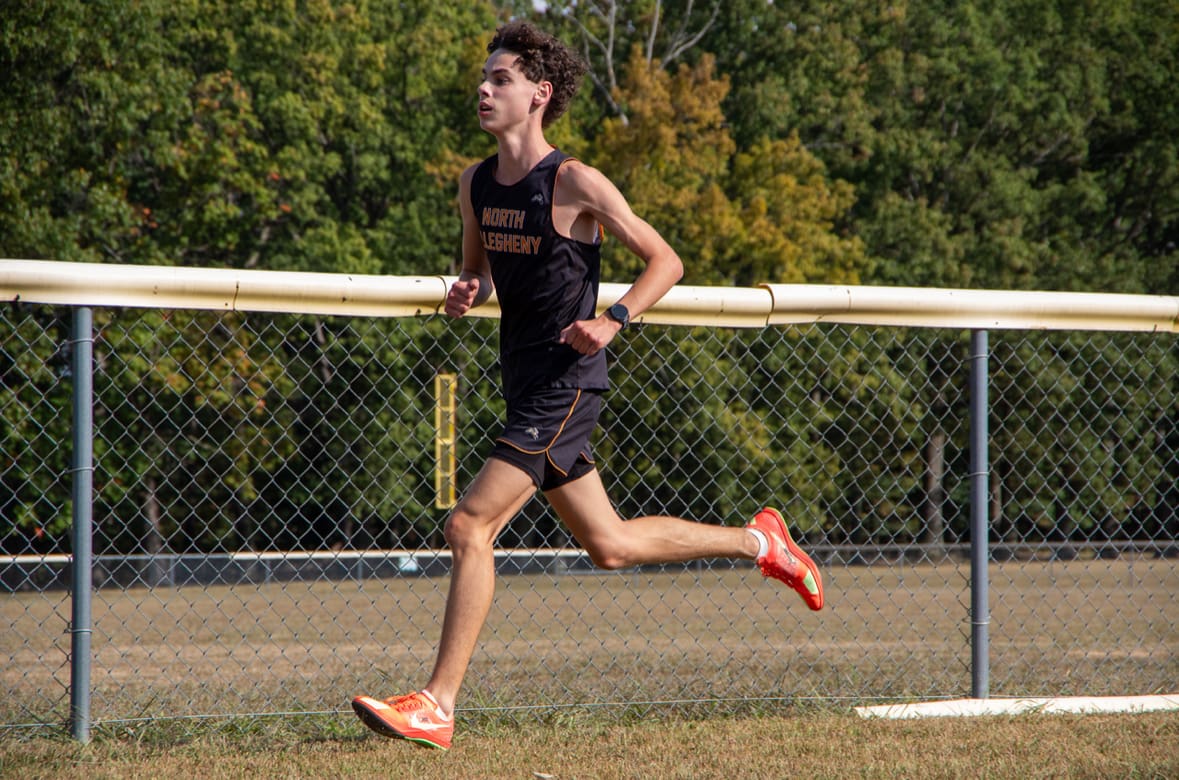 Runner in a black sports outfit running by a fence in a park during a sunny day.
