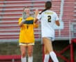 Two female soccer players high-five on the field, one in yellow, one in white with Tigers on the back.