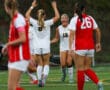 Soccer players in action, celebrating a goal on the field during a match, wearing red and white uniforms.