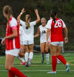 Soccer players in action, celebrating a goal on the field during a match, wearing red and white uniforms.
