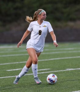 Soccer player in white uniform dribbling ball on field during a game.