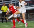 Two female soccer players competing for the ball during a match on a green field.