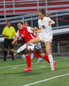 Two female soccer players competing for the ball during a match on a green field.