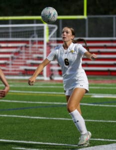 Soccer player in white jersey number 6 skillfully controls ball on field during match at night game.