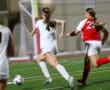 Two female soccer players in action on the field during a night game, sprinting towards the ball.