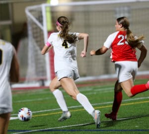 Two female soccer players in action on the field during a night game, sprinting towards the ball.