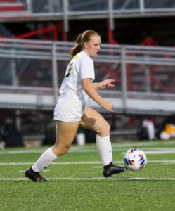Soccer player in white uniform running with ball on grass field during match.