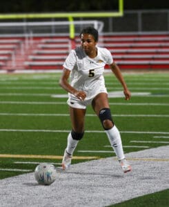 Soccer player in white uniform dribbles ball on field during night game.