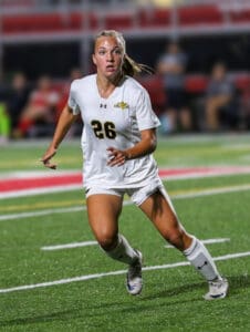 Soccer player in white uniform running on field during a match, wearing the number 26.