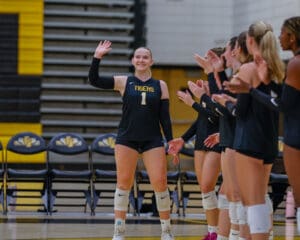Volleyball player in a Tigers uniform waves while teammates applaud in a sports hall.