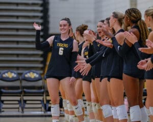 Volleyball team players in black uniforms clapping and celebrating on the court.