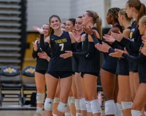 Volleyball team players in black uniforms applauding a teammate during a match in a gym.