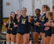 Volleyball team huddle with player number 12 waving and teammates clapping, wearing Tigers jerseys in gym setting.