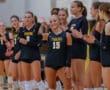Volleyball team lining up, player number 15 waves and smiles, others clapping, wearing black Tigers jerseys.