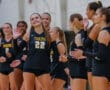 Women's volleyball team celebrates during a match, smiling player number 22 waves.
