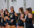 Volleyball team wearing black uniforms, one player waving and smiling, showing team spirit before a match.
