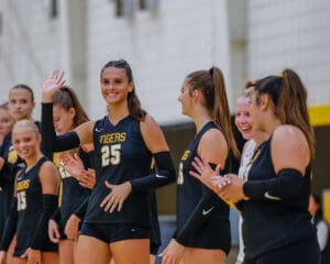 Volleyball team wearing black uniforms, one player waving and smiling, showing team spirit before a match.