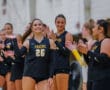 Volleyball players in Tigers jerseys celebrate, smiling and clapping during a match indoors.