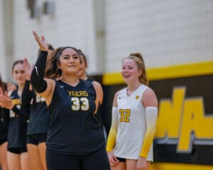 Volleyball players in black and white jerseys smiling and clapping during a game in a gymnasium.