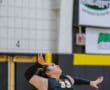 Volleyball player in black jersey preparing to serve during a game in an indoor court.