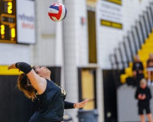 Volleyball player performs a powerful serve in an indoor court, showcasing athleticism and focus.