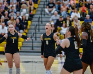 College volleyball team celebrates a point during a home game, with cheering fans in the background.