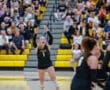 Female volleyball player celebrating a point on the court, in front of cheering crowd and yellow bleachers.