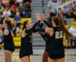 Volleyball team celebrating a point during a game in a gym with spectators in the background.