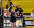 Volleyball player in action, setting the ball during a match in a gym with yellow bleachers. Player wears Tigers jersey.