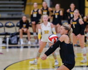 Volleyball player in black uniform preparing to hit the ball during a game in an indoor court.