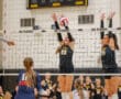 Volleyball match action with NA Tigers players blocking at the net against Titans player preparing to hit the ball.
