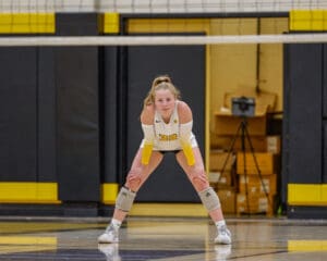 Volleyball player in ready stance on indoor court during game.