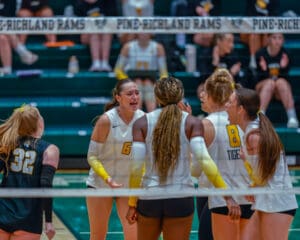 Volleyball team celebrates after scoring a point during a high school match in a gym.
