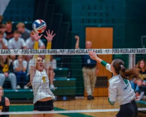 Girls playing volleyball at Pine-Richland Rams match, athlete in action blocking a spike over the net.