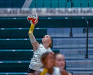 Volleyball player in action, preparing to serve during a match in an indoor sports arena.