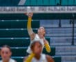 Volleyball player preparing to spike the ball during a game in an indoor arena.