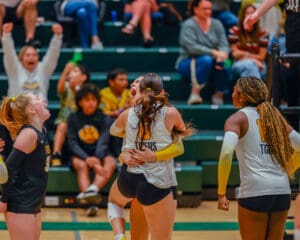 Volleyball team celebrates a victory as audience cheers in the background, showcasing team spirit and excitement.