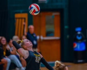 Volleyball player in mid-jump preparing to spike the ball during an indoor match.