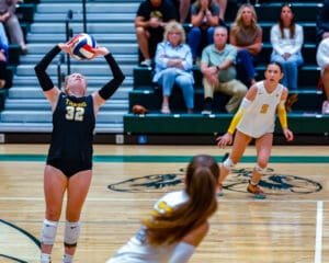 Volleyball player setting the ball during a game with teammates and spectators in the background.